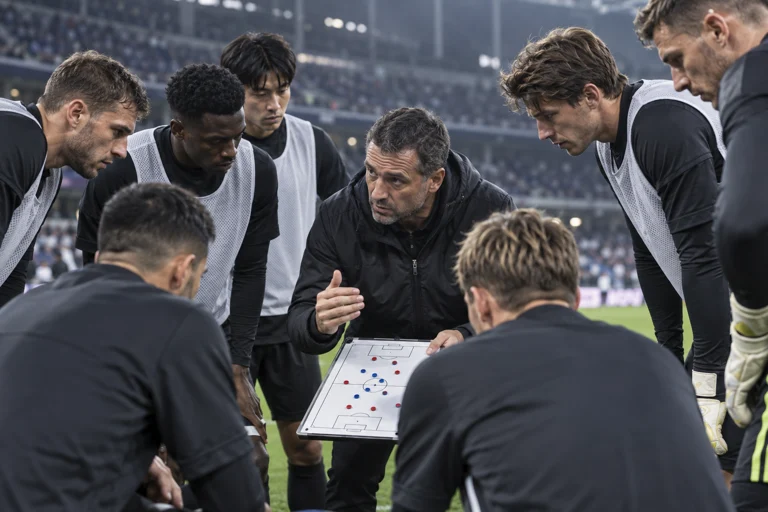 足球队赛前进行战术讨论，背景为灯光明亮的体育场看台